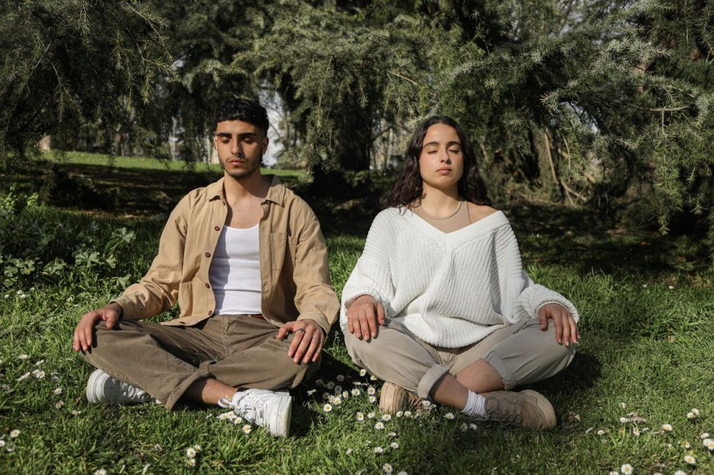 Two individuals meditating in a serene park setting. Peaceful and relaxed environment.